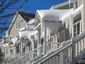 a home in winter with snow on roof, large icicles hanging that may be from an ice dam